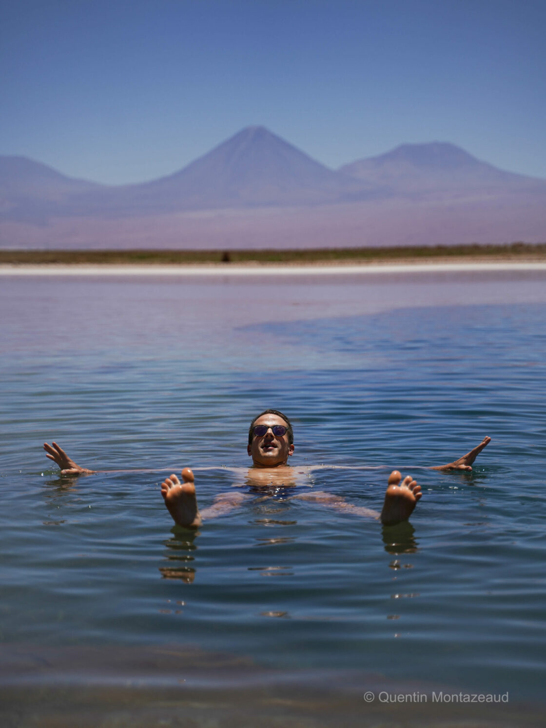 Laguna Cejar Atacama Person floating on the turquoise waters of Laguna Cejar, surrounded by salt flats under a clear sky.